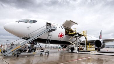 An Air Canada cargo jet with black underbelly gets loaded through side door.