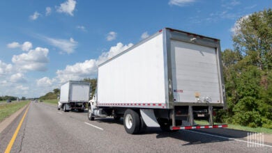 Two white, last-mile trucks on a highway