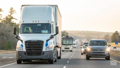 White semi-truck driving on a road with passenger cars in the next lane