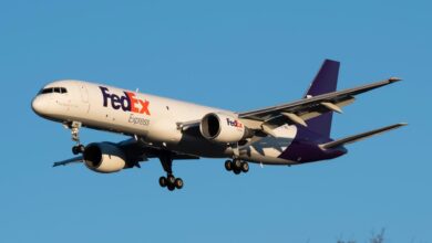 A purple-tailed FedEx plane approaches landing with wheels down.