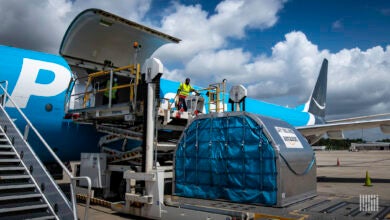 A light blue Amazon Prime plane on the ground with its side cago door open and a container ready to be loaded from the ground.