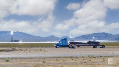 A blue tractor pulling a covered flatbed trailer