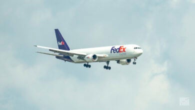 A purple-tail FedEx jet with wheels down on approach to an airport.