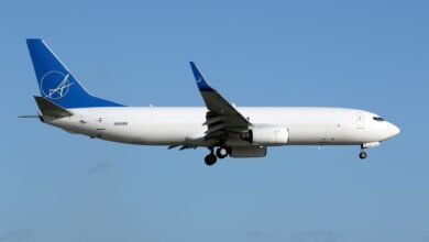 A blue-tailed white jet approaches an airport with wheels down. View from the side.