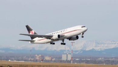 A blue-tailed Cargojet aircraft takes off with snow-covered mountains in the background.