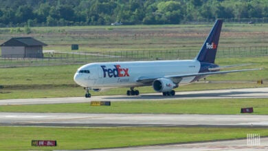 A purple-tailed FedEx cargo jet on a taxiway with grass fields around it.