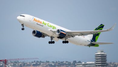 An Aloha Air Cargo jetliner with green accents takes off from LAX with building in background.