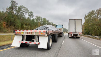 A covered flatbed trailer next to a dry van trailer on a highway