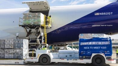 Close up side view of cargo being lifted from a ground vehicle into a blue-and-white cargo jet.