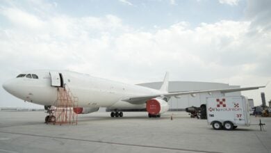 All white cargo jet sits in front of an airport hangar.