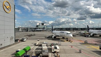 A Lufthansa passenger jet pulls into a terminal gate area on a sunny day.