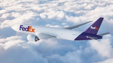 A purple-tail FedEx cargo jet flies above above white clouds.