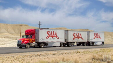 A red Saia tractor pulling three Saia LTL trailers in the desert