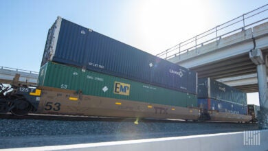 Image shows containers on doublestack railcar under highway bridge.