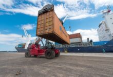 Image shows a container ship, containers and reach stacker.