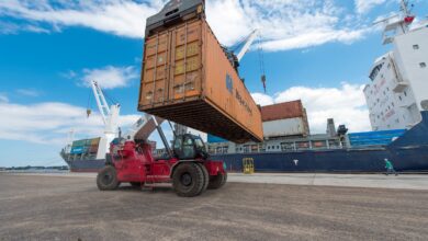 Image shows a container ship, containers and reach stacker.