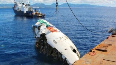 Cranes pull a fuselage out of the sea onto a barge.