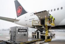 A black-tailed jet with red Canadian maple leaf is loaded with a container on a snowy day.