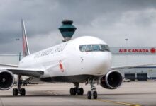 Frontal view of an Air Canada Cargo jet with cargo terminal in the background.