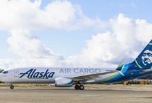 An Alaska Air Cargo plane taxis on the runway on a sunny day. Side view.