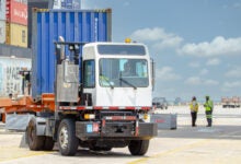 A yard tractor pulls a container on a chassis at a port.