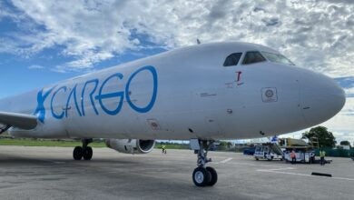 Close up, right-side view of GlobalX Cargo plane with blue lettering on a sunny day with white clouds above.