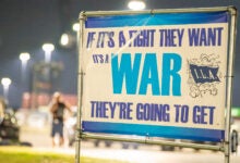 Image shows a longshore union sign that says "If it's a fight they want it's a war they're going to get"