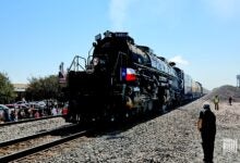 Image shows a steam locomotive, blue sky, people trackside.