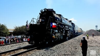 Image shows a steam locomotive, blue sky, people trackside.