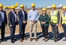 Men and women in yellow vests and hats at an airport groundbreaking event.