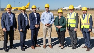 Men and women in yellow vests and hats at an airport groundbreaking event.