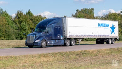 A blue sleeper cab pulling a white Landstar trailer on a highway