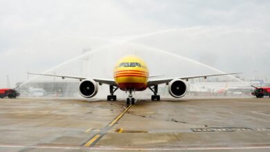 A mustard-yellow cargo jet drives under two streams of water from fire trucks to celebrate an inaugural flight.