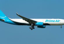 Light-blue tailed Amazon Prime Air jet with wheels down for landing against blue sky.