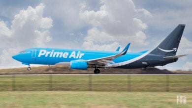 A light blue Prime Air cargo jet for Amazon lands on a runway.