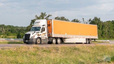 A white Schneider daycab pulling an orange Schneider dryvan trailer on a highway