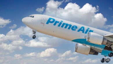 Close up side view of a Prime Air jet by Amazon with light blue lettering taking off with white clouds in background.