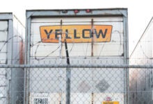 A Yellow trailer parked along a fence at a terminal in Houston