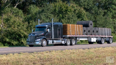 A black sleeper cab pulling a loaded flatbed trailer on a highway