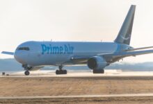 An Amazon Prime Air cargo jet with blue markings rolls forward on runway.