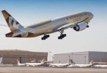 An Etihad Cargo jet with multicolored tail takes off with hangar buildings in the background.