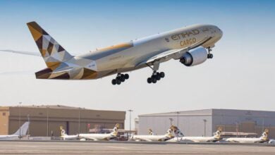 An Etihad Cargo jet with multicolored tail takes off with hangar buildings in the background.