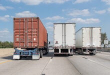 Rearview of one ocean container and two trailers being pulled on a highway