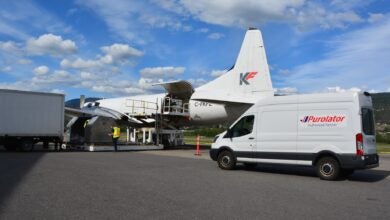 A Purolator delivery van on an airport tarmac next to a propeller cargo aircraft.