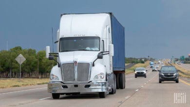 A white sleeper cab pulling a blue ocean container on a highway