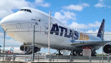 Front close up of an Atlas Air jumbo jet from behind a fence line.