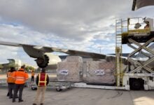 Cargo being loaded with hydraulic lifts onto a plane. View from below the wing.