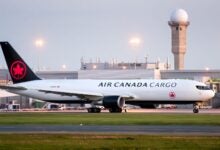 Side view of black-tailed Air Canada Cargo jet with red maple leaf at airport.