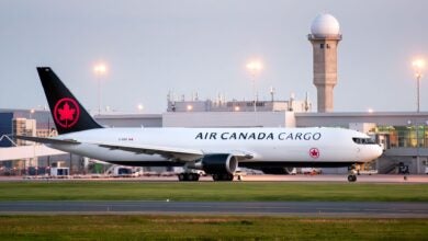 Side view of black-tailed Air Canada Cargo jet with red maple leaf at airport.