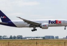 A purple-tail FedEx jet with wheels down for runway landing.